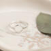 Single open circle sterling silver ring on white marbled dish with green leaf.

